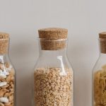 Three clear glass jars with cork lids hold beans, lentils, and pasta showcasing pantry organization.